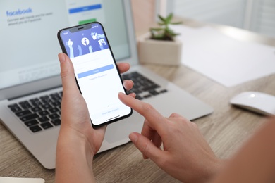 MYKOLAIV, UKRAINE - AUGUST 28, 2020: Woman holding iPhone 11 with Facebook app on screen at table, closeup