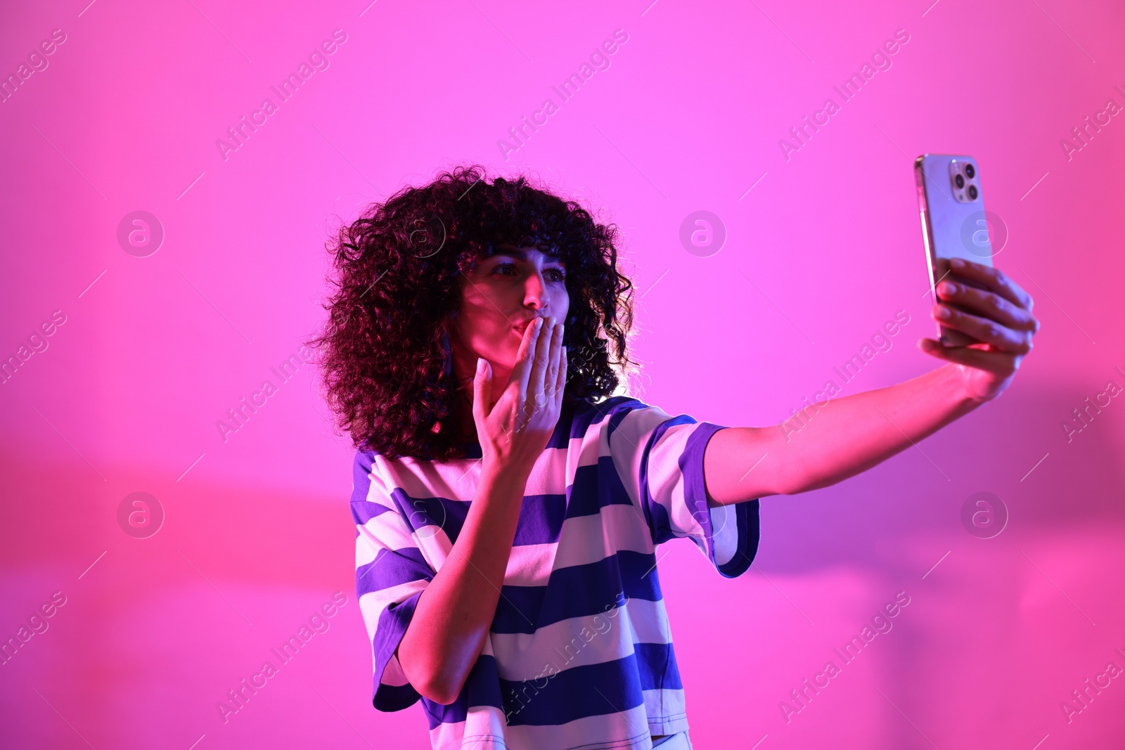 Photo of Beautiful young woman taking selfie on color background in neon lights