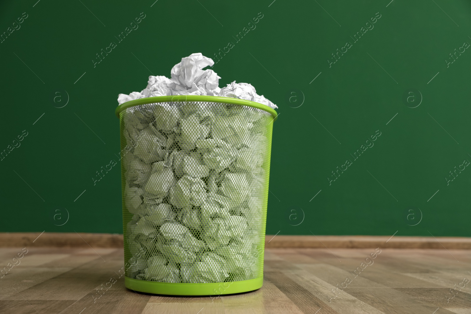 Photo of Metal bin with crumpled paper on floor against color wall, space for text