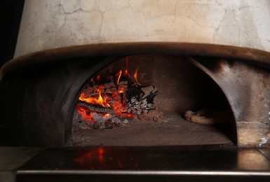 Oven with burning firewood and tasty pizza in restaurant kitchen