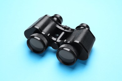 Photo of Modern binoculars on light blue background, closeup