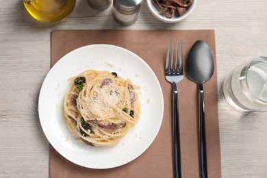 Delicious pasta with anchovies, olives and parmesan cheese served on light wooden table, flat lay