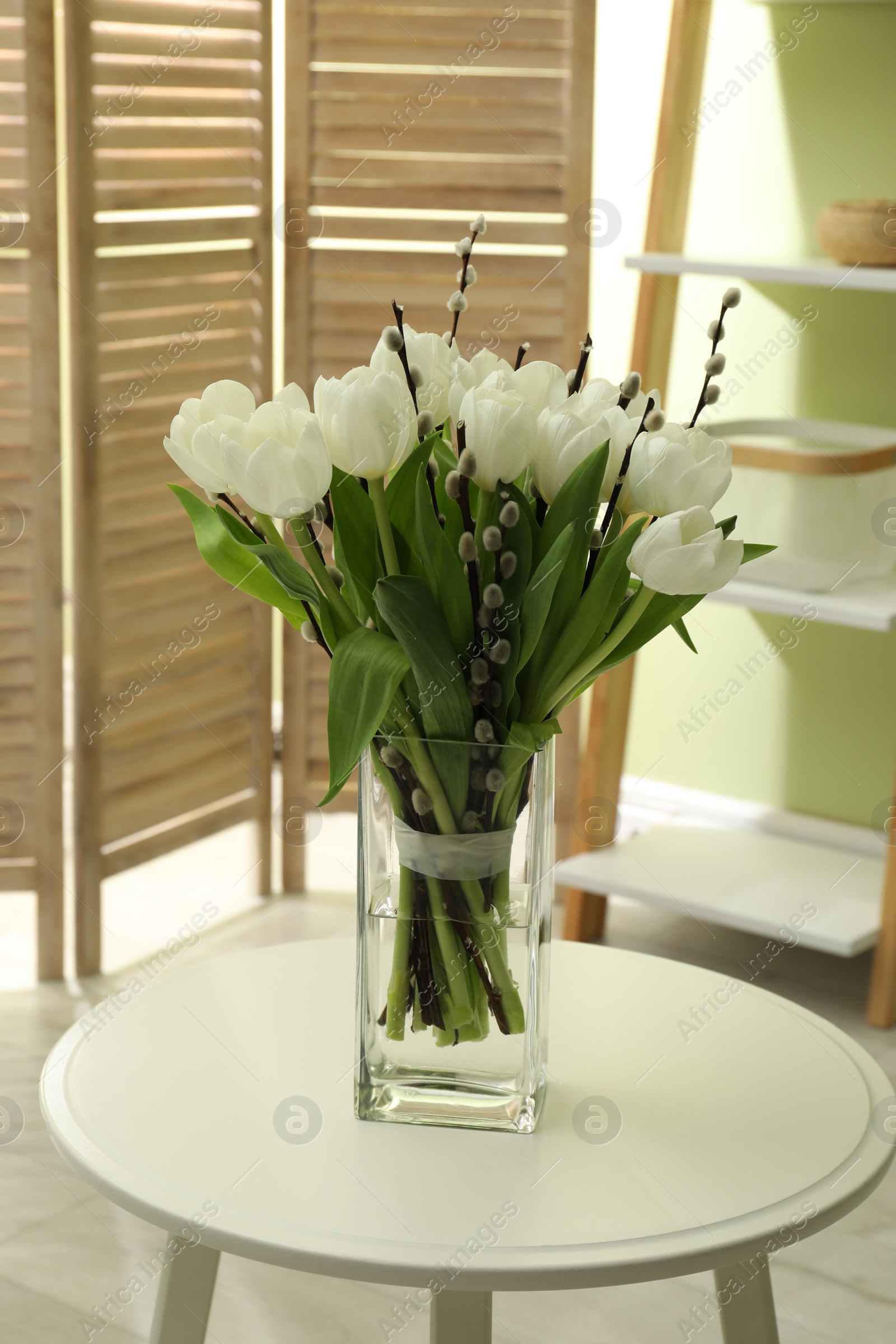 Photo of Beautiful bouquet of willow branches and tulips in vase on table indoors