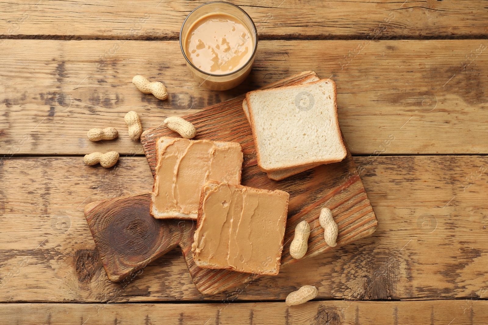 Photo of Tasty peanut butter sandwiches and peanuts on wooden table, flat lay