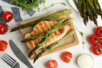 Photo of Tasty grilled chicken fillet served with asparagus and sprouts on white wooden table, flat lay