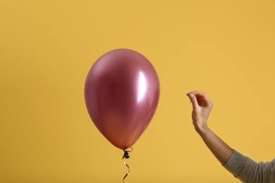 Woman piercing balloon with needle on color background, closeup