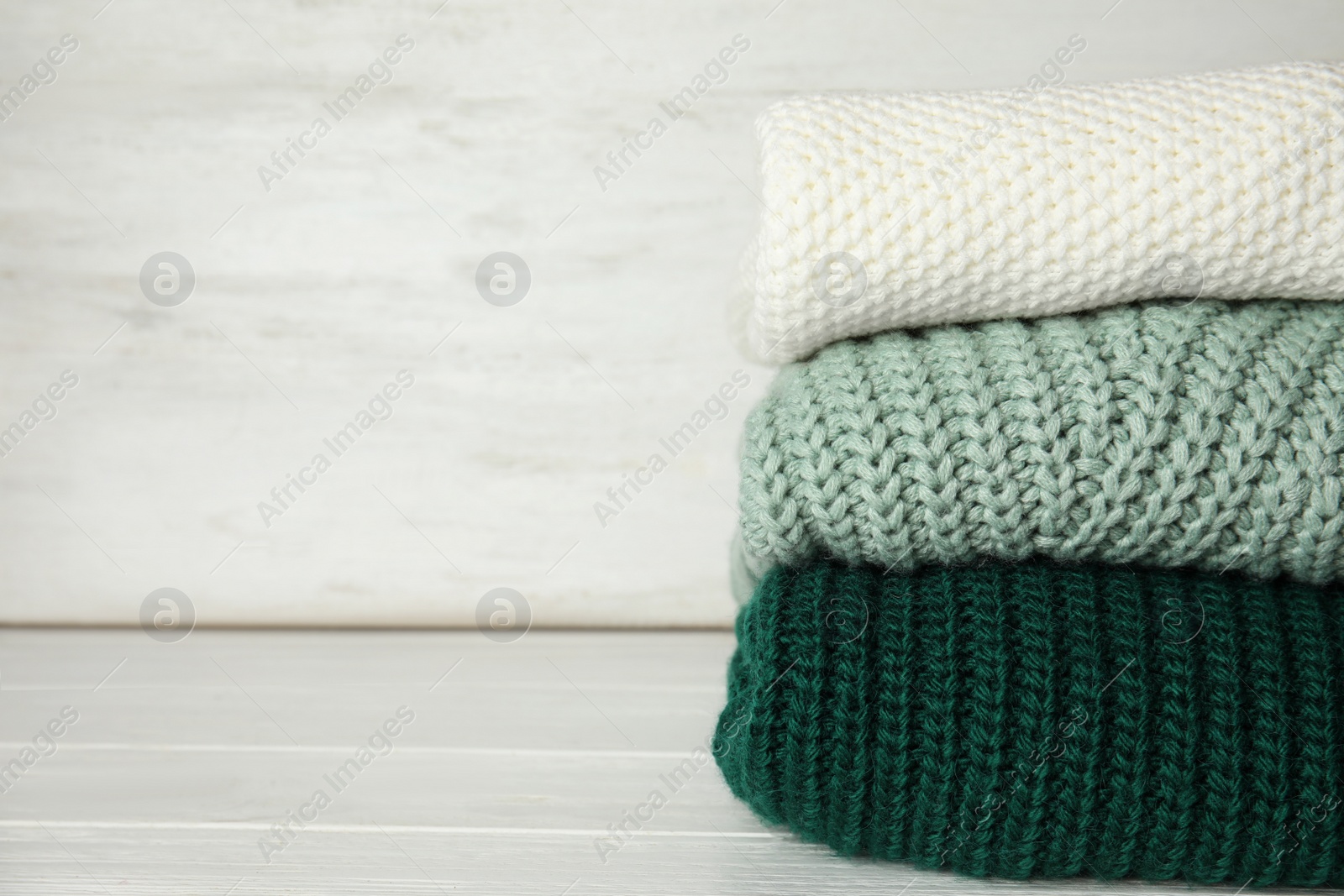 Photo of Stack of knitted clothes on white wooden background, space for text. Cozy autumn