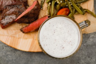 Mug with beer, delicious fried steak and asparagus on grey table, closeup. Space for text