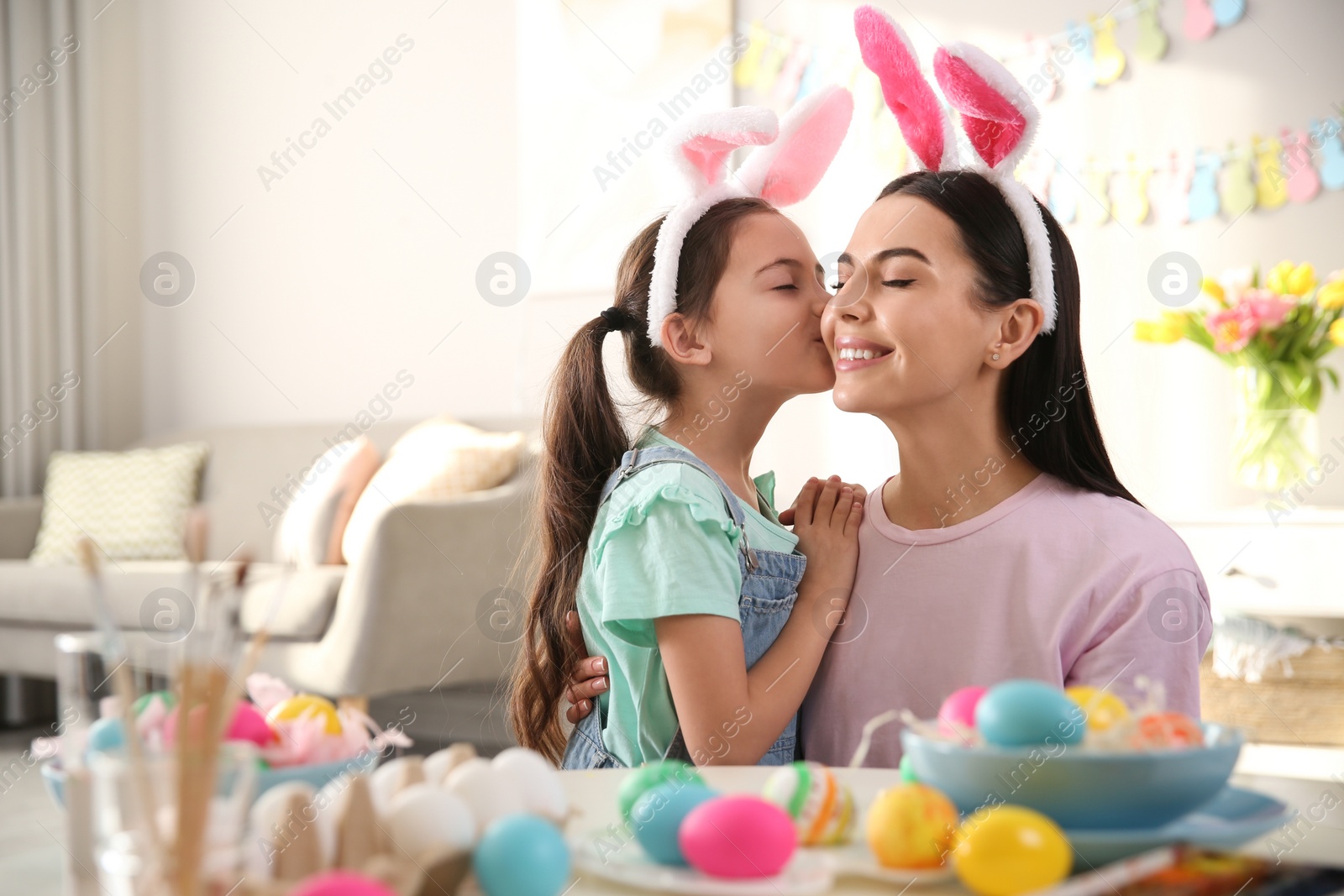 Photo of Happy mother with her cute daughter painting Easter eggs at table indoors