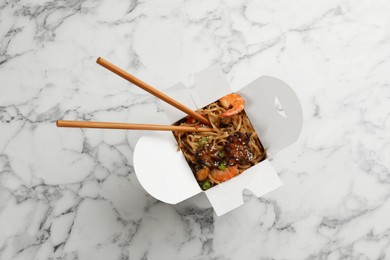 Photo of Box of wok noodles with seafood and chopsticks on white marble table, top view