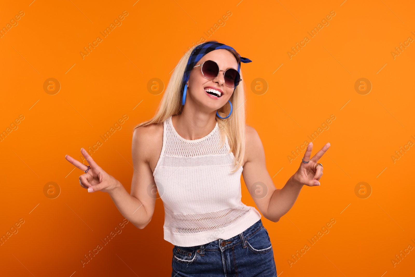 Photo of Smiling hippie woman showing peace signs on orange background