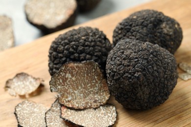 Photo of Whole and cut black truffles on wooden board, closeup