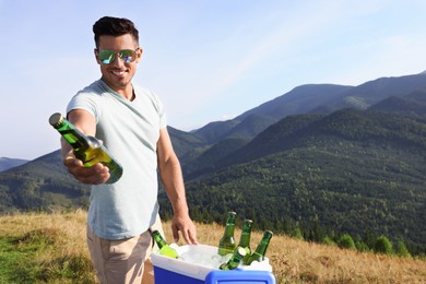 Man giving bottle from cool box in mountains. Space for text