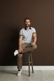 Photo of Handsome man sitting on stool near brown wall