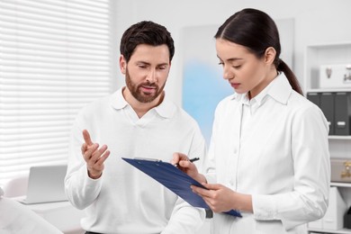 Photo of Doctor with clipboard consulting patient during appointment in clinic