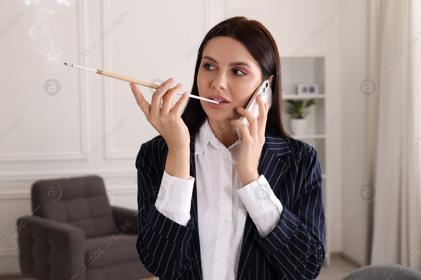 Photo of Woman using long cigarette holder for smoking and talking on phone in office