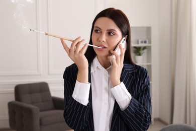 Woman using long cigarette holder for smoking and talking on phone in office