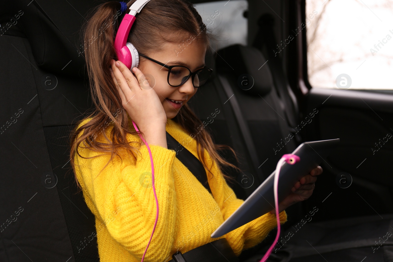 Photo of Cute little girl listening to audiobook in car