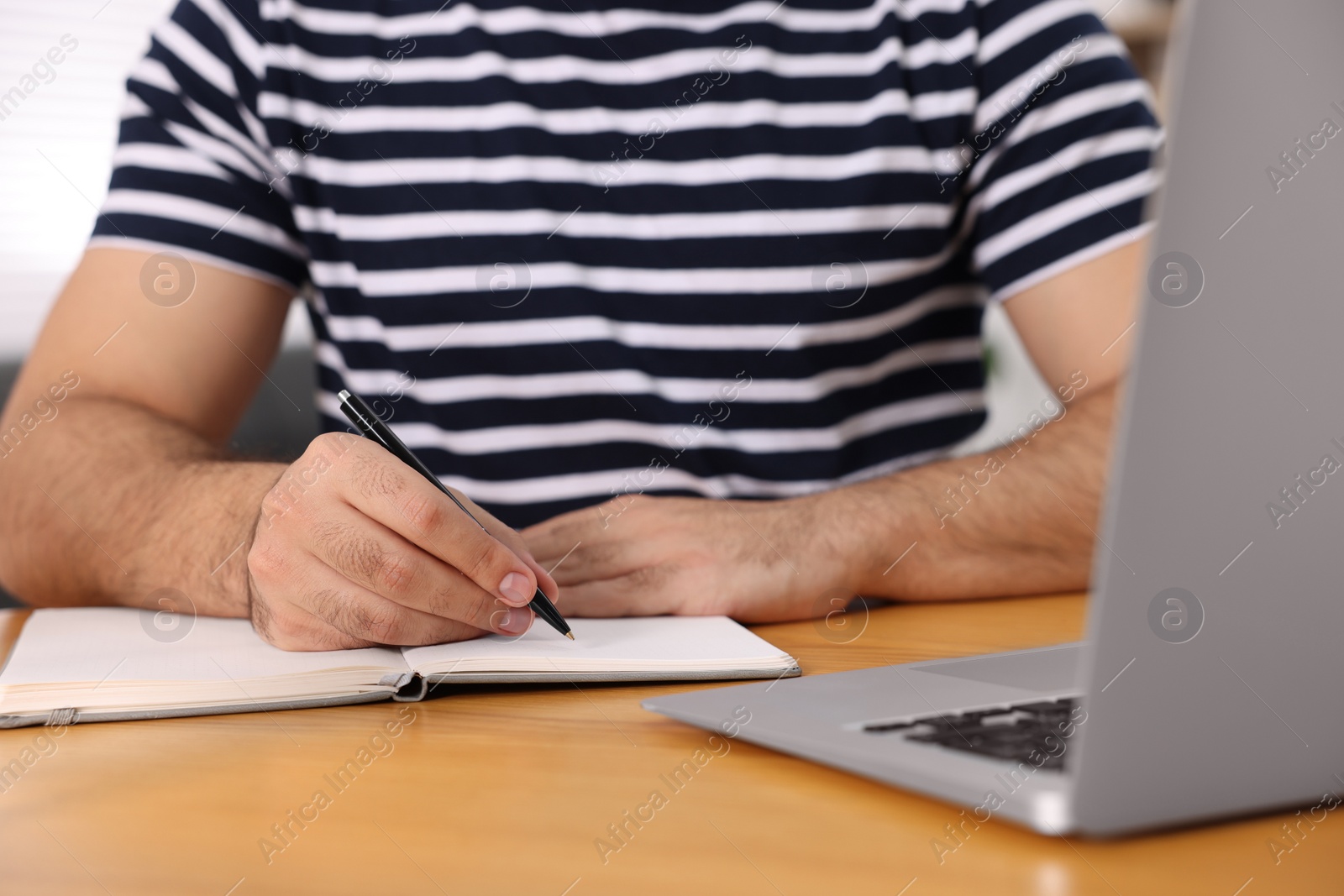 Photo of Young man writing in notebook at wooden table, closeup