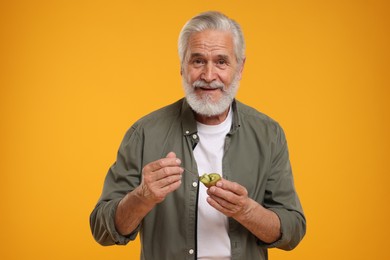 Photo of Senior man eating kiwi with spoon on yellow background