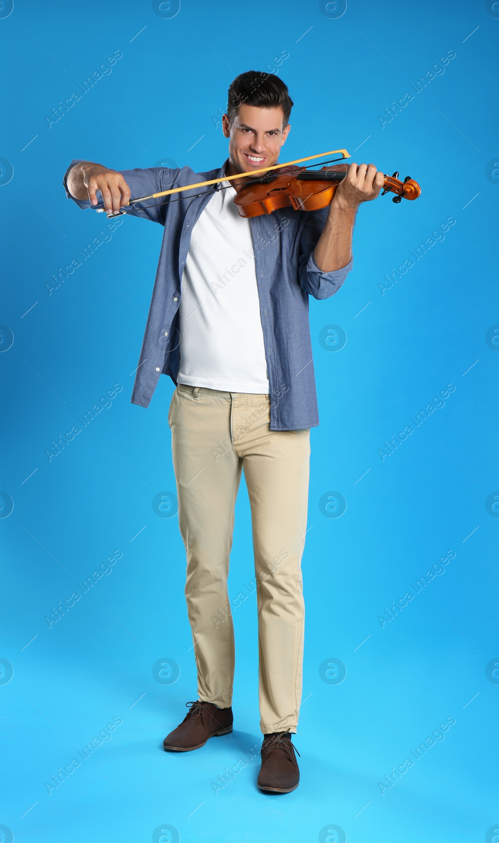 Photo of Happy man playing violin on light blue background