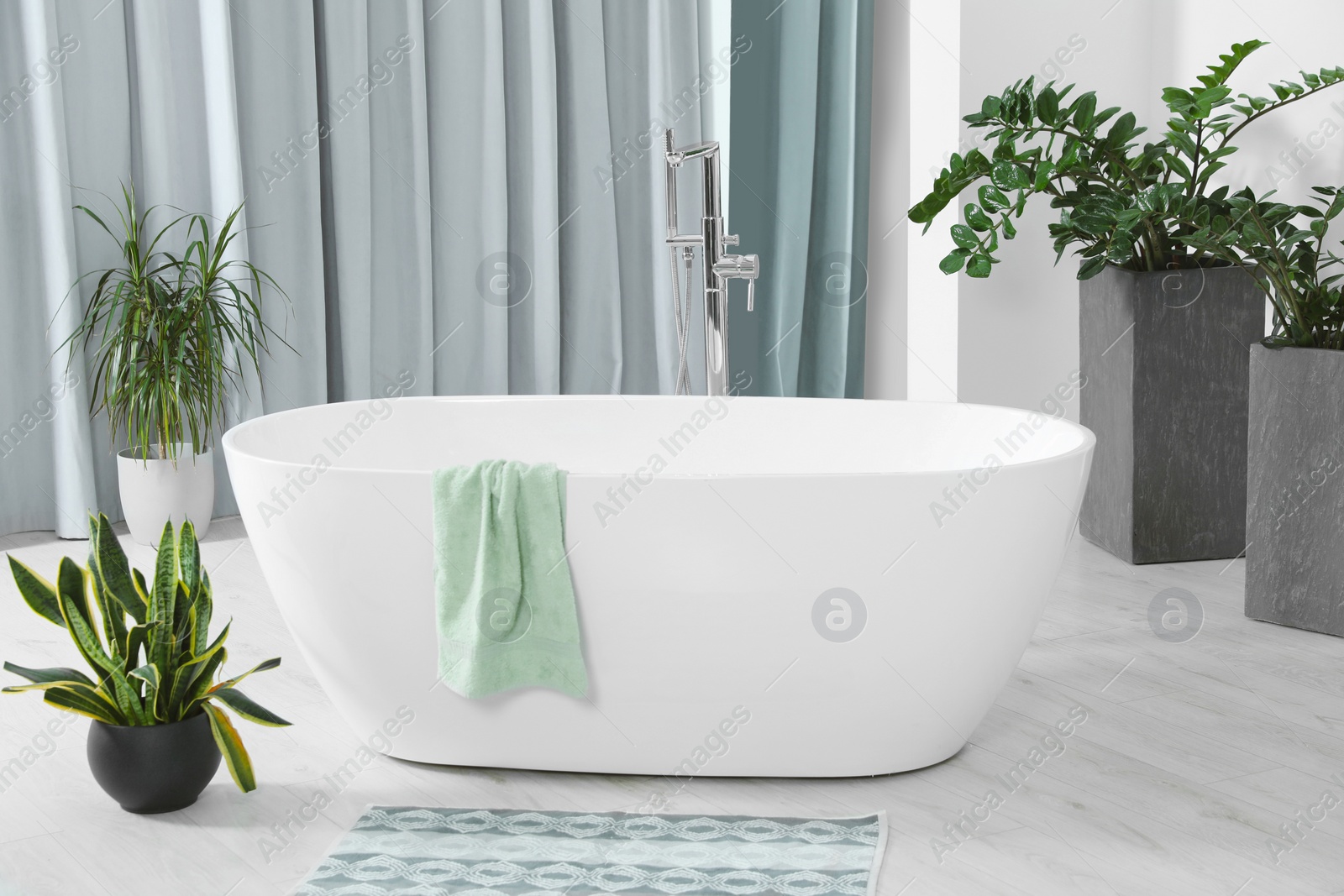 Photo of Stylish white tub and green houseplants in bathroom. Interior design