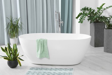 Stylish white tub and green houseplants in bathroom. Interior design