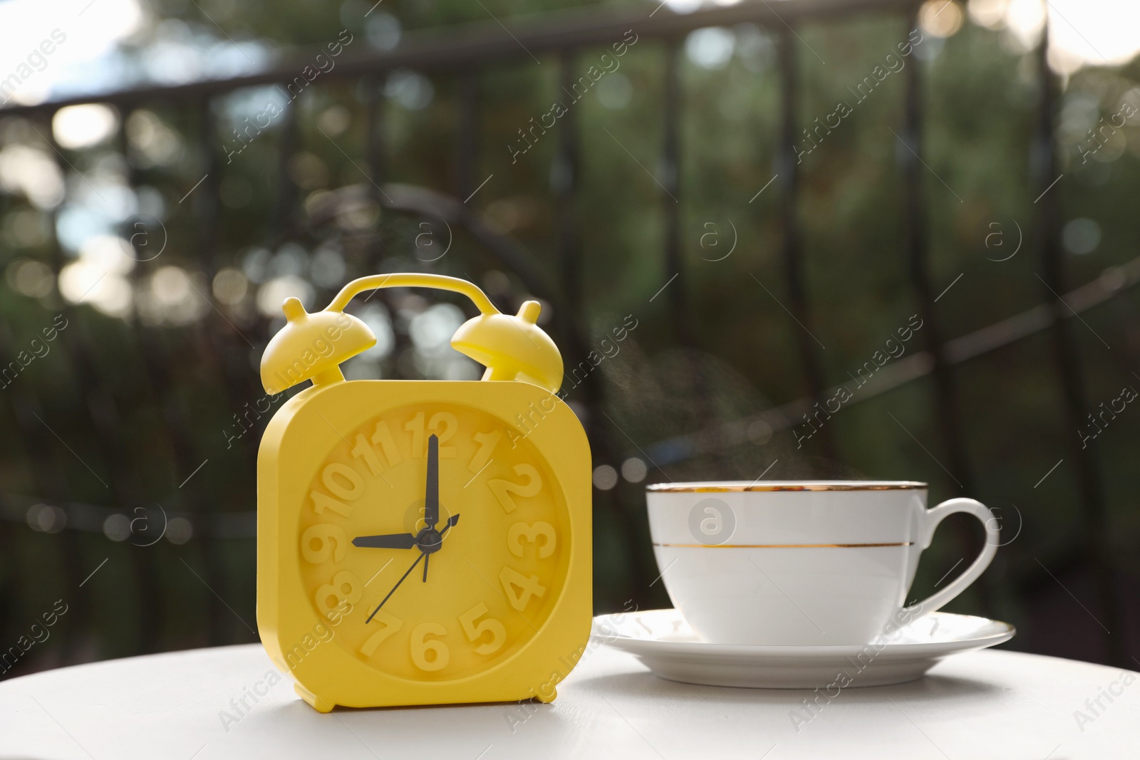 Photo of Yellow alarm clock and cup with hot drink on white table in morning