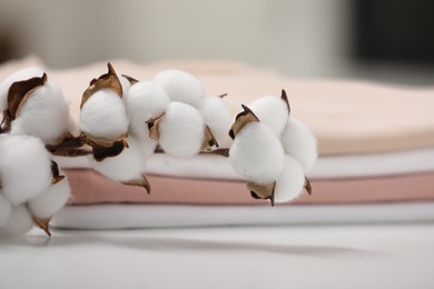 Photo of Bed sheets and cotton branch with fluffy flowers on white table, closeup