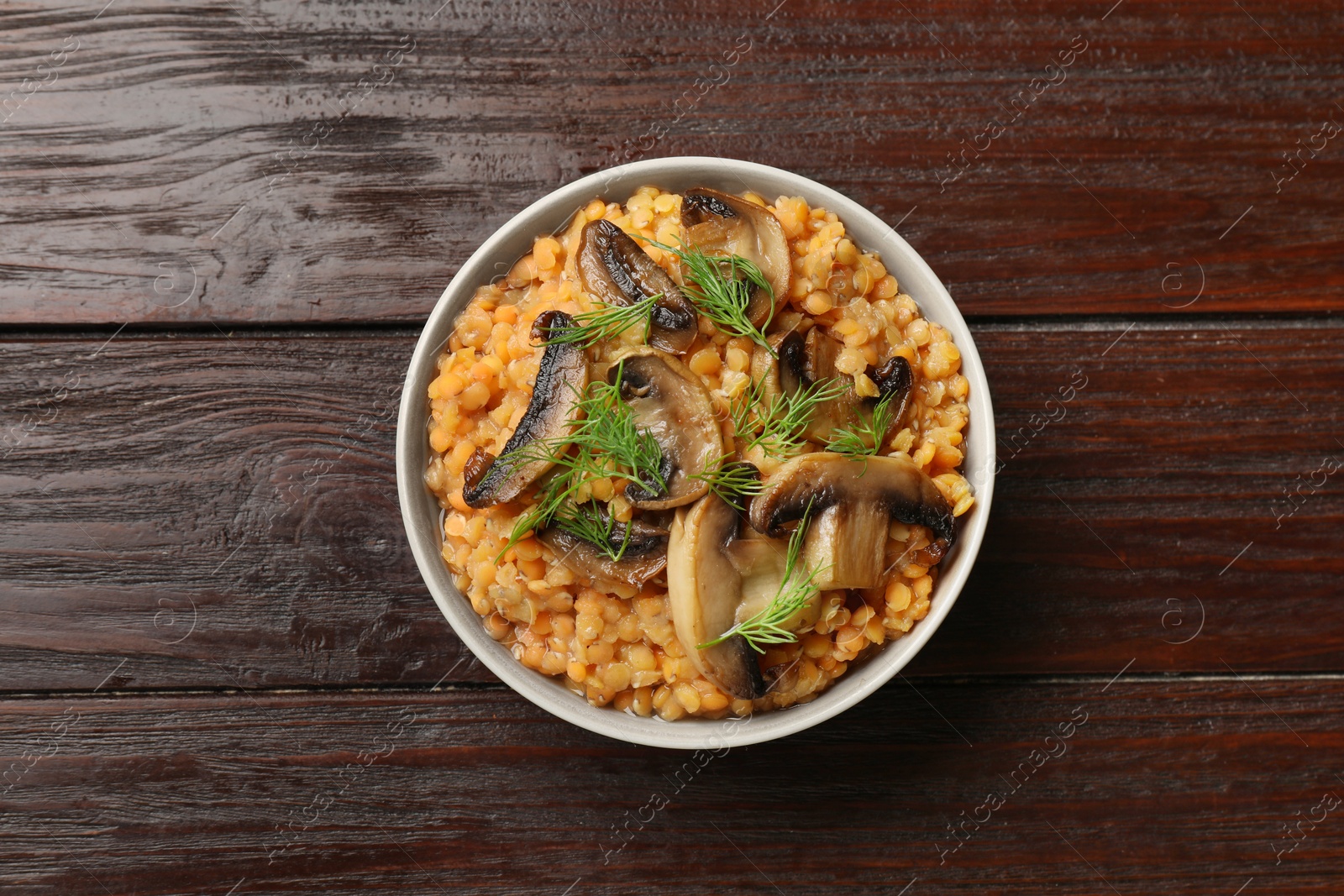 Photo of Delicious red lentils with mushrooms and dill in bowl on wooden table, top view