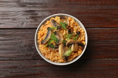 Photo of Delicious red lentils with mushrooms and dill in bowl on wooden table, top view