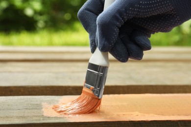 Woman painting wooden surface with coral dye outdoors, closeup