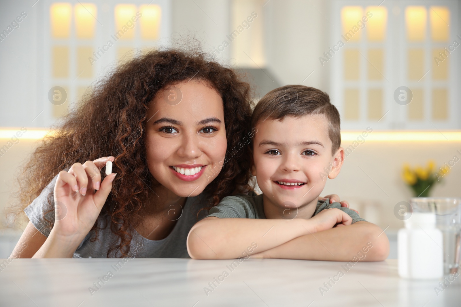 Photo of African-American woman and little boy with vitamin pill in kitchen