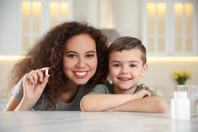 Photo of African-American woman and little boy with vitamin pill in kitchen