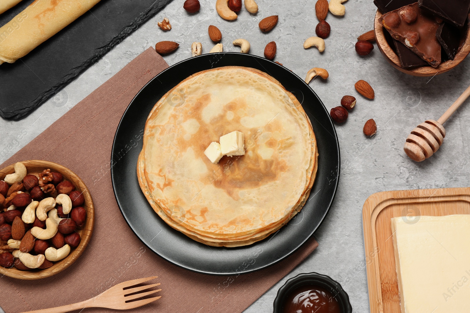 Photo of Delicious crepes with butter, chocolate and nuts on light grey table, flat lay