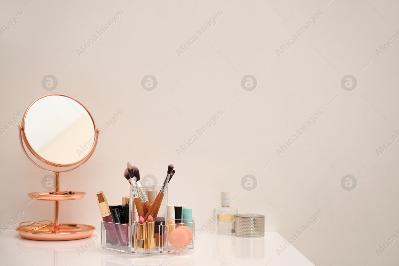 Photo of Makeup cosmetic products and tools in organizer on dressing table near color wall with space for text