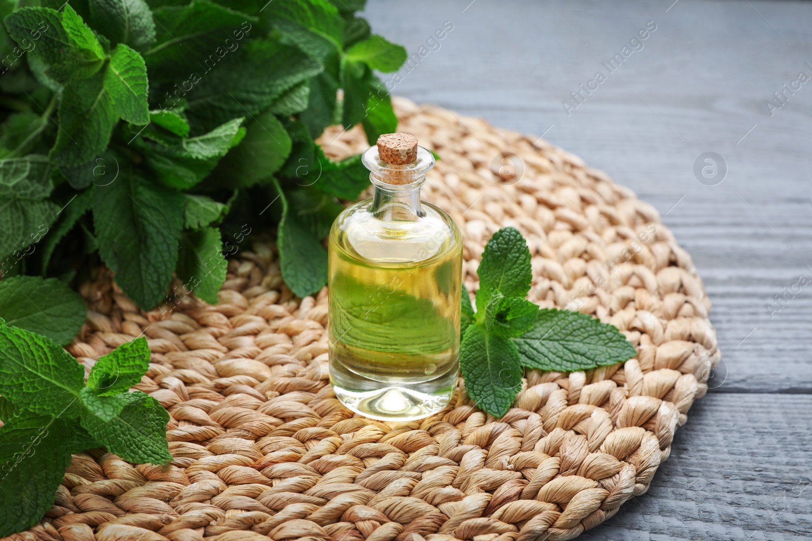 Photo of Bottle of essential oil and mint on grey wooden table, closeup