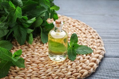 Photo of Bottle of essential oil and mint on grey wooden table, closeup