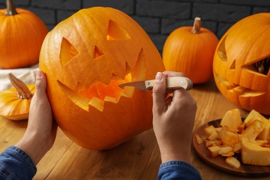 Photo of Woman carving pumpkin at wooden table, closeup. Halloween celebration