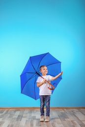 Photo of Little boy with blue umbrella near color wall. Space for text