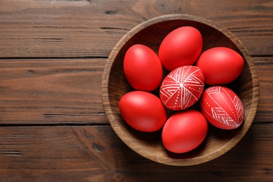 Photo of Wooden bowl with painted red Easter eggs on table, top view. Space for text