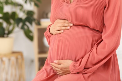 Pregnant woman in coral dress at home, closeup