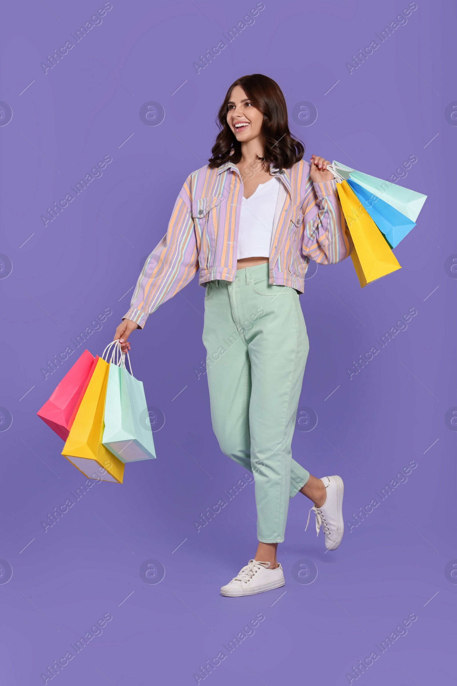 Photo of Beautiful young woman with paper shopping bags on purple background