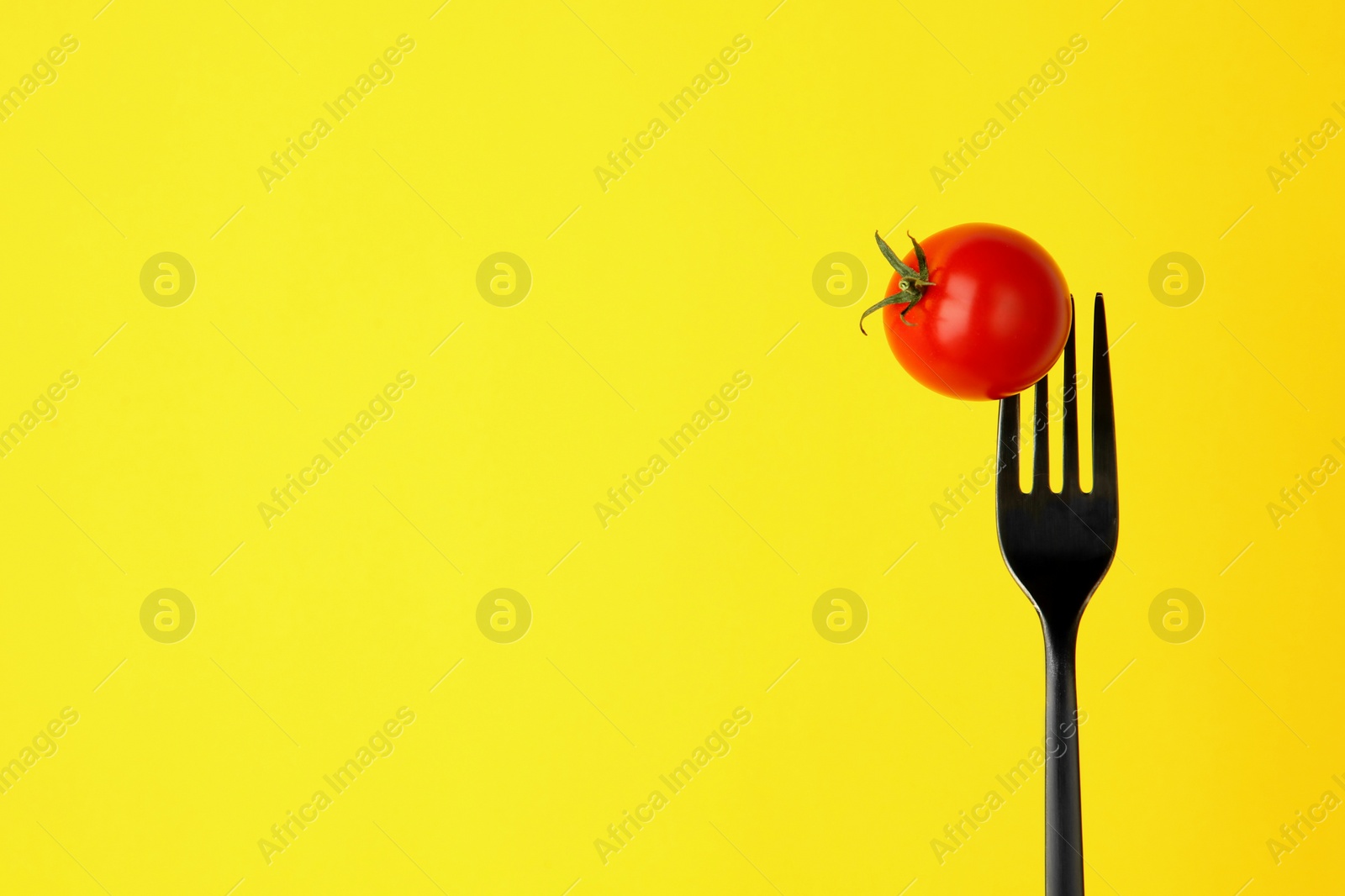 Photo of Fork with cherry tomato on yellow background, space for text