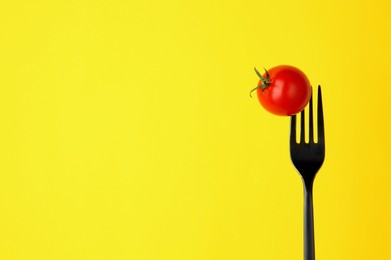 Fork with cherry tomato on yellow background, space for text