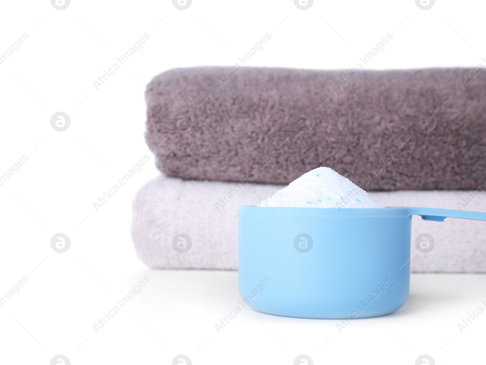 Photo of Laundry detergent in plastic measuring scoop and towels on white background