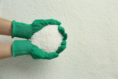 Photo of Woman holding pile of granular mineral fertilizer over grains, top view. Space for text