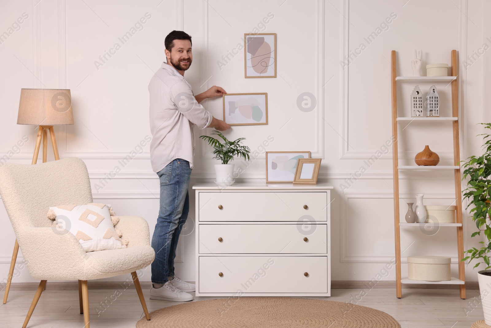 Photo of Man hanging picture frame on white wall at home