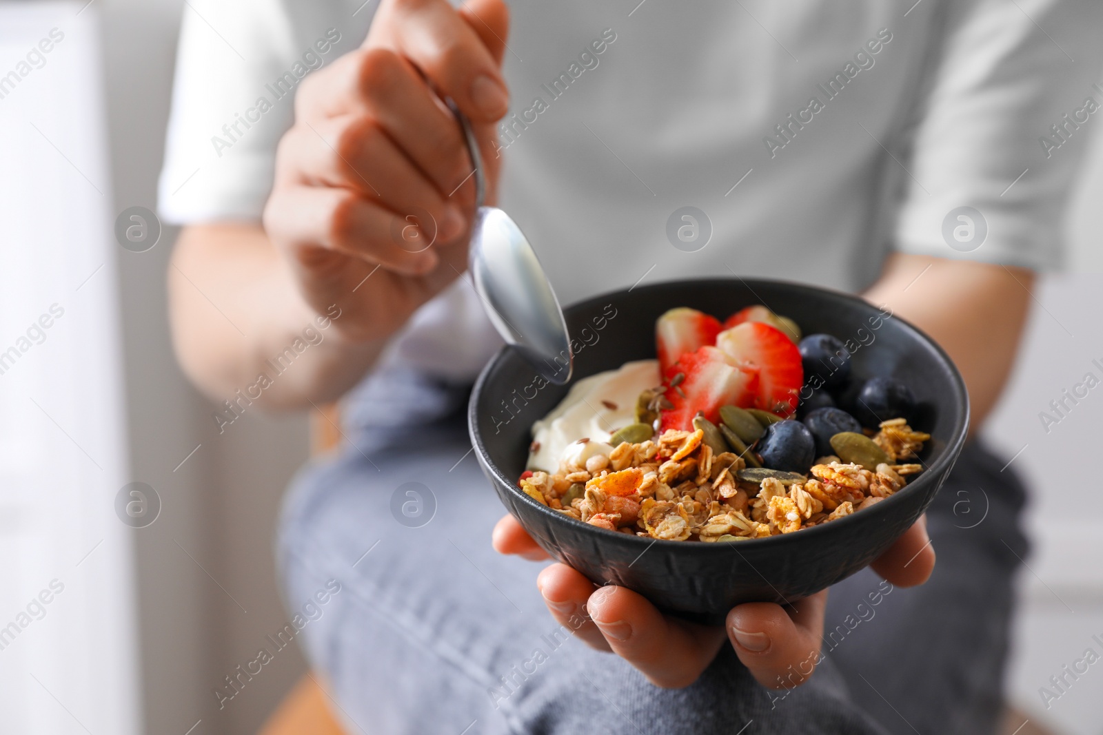 Photo of Woman eating tasty granola with berries, yogurt and seeds indoors, closeup