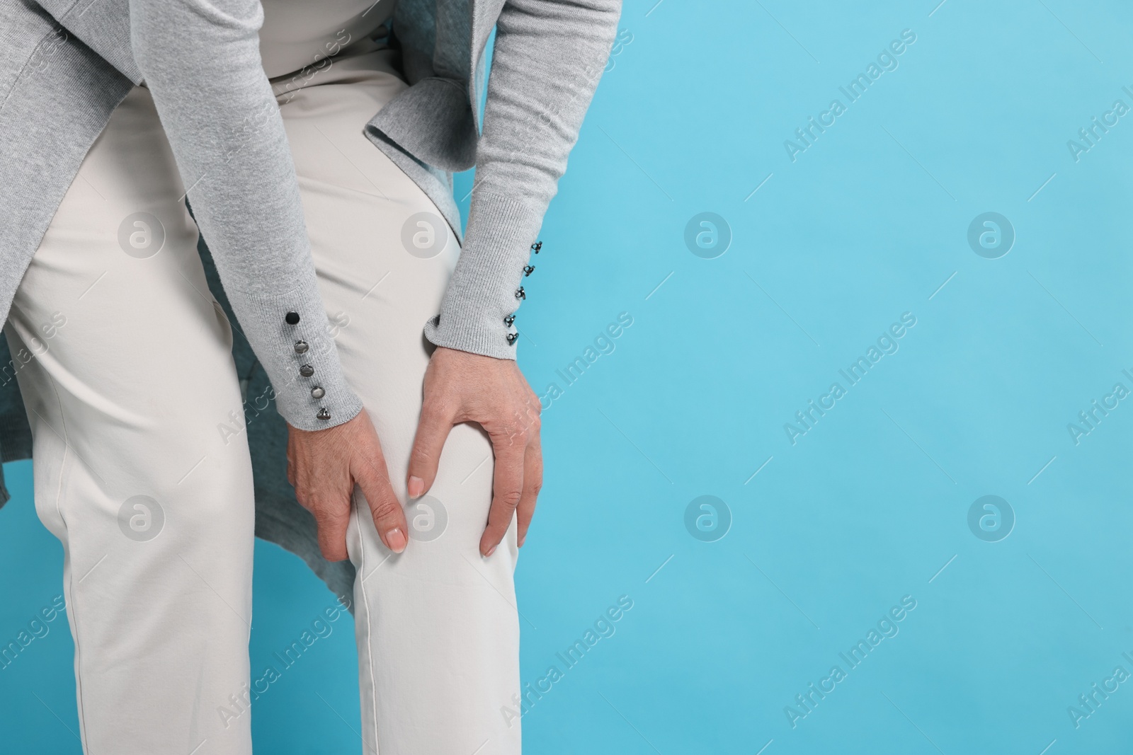 Photo of Arthritis symptoms. Woman suffering from pain in knee on light blue background, closeup. Space for text